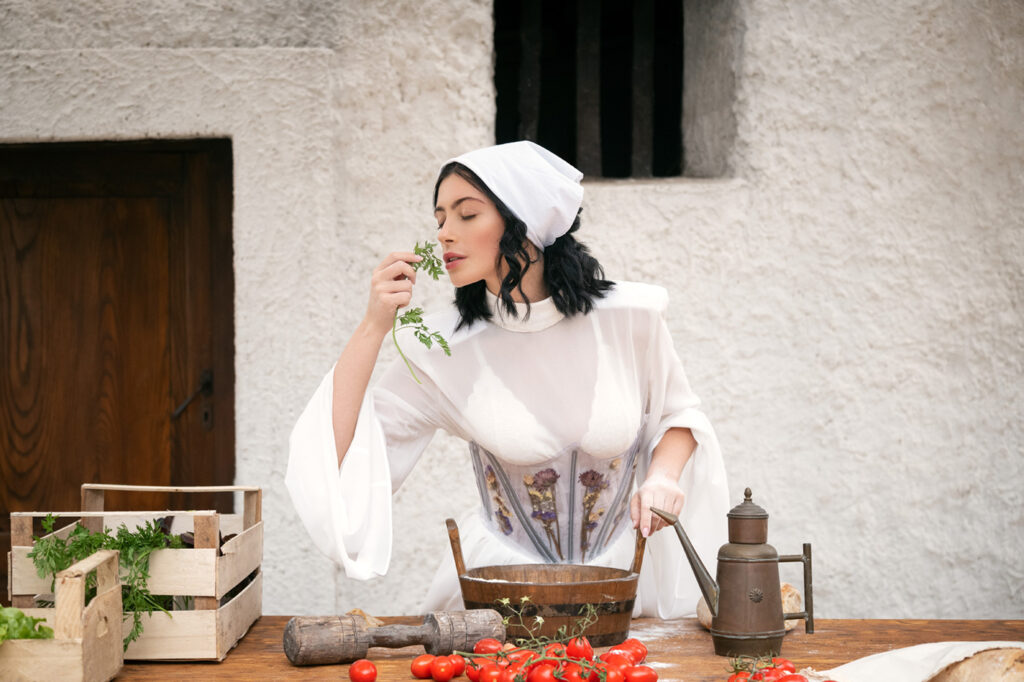 Woman preparing food with herbs and tomatoes, fashion editorial shot in Italy